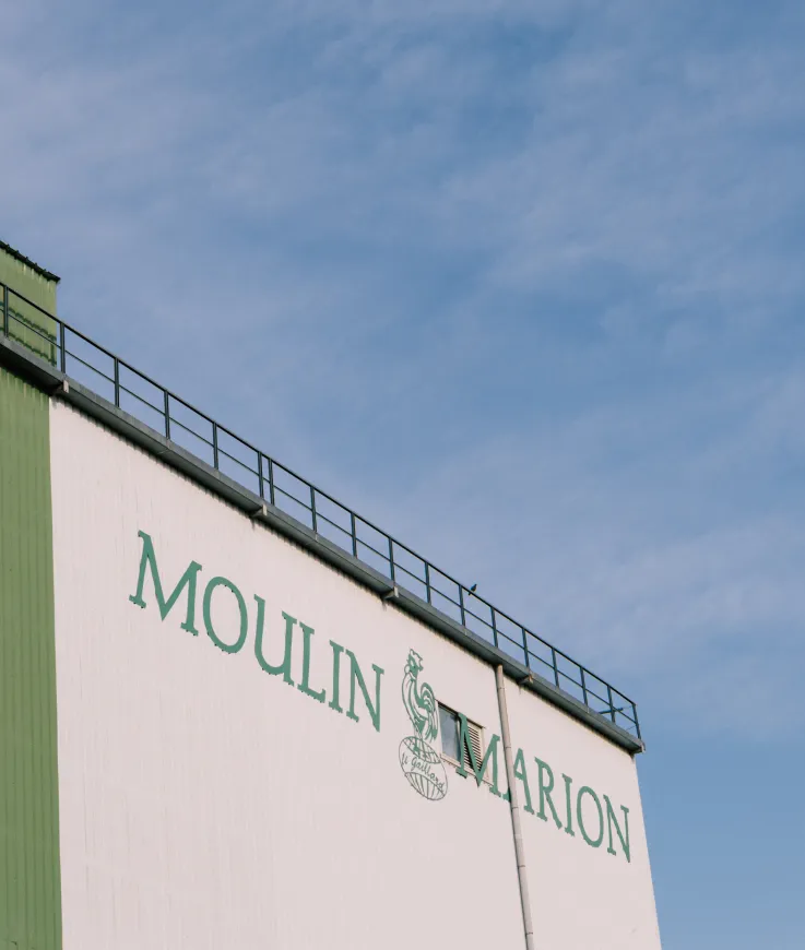 Pignon du moulin Marion portant l'enseigne Moulin Marion et son coq, sous un ciel bleu